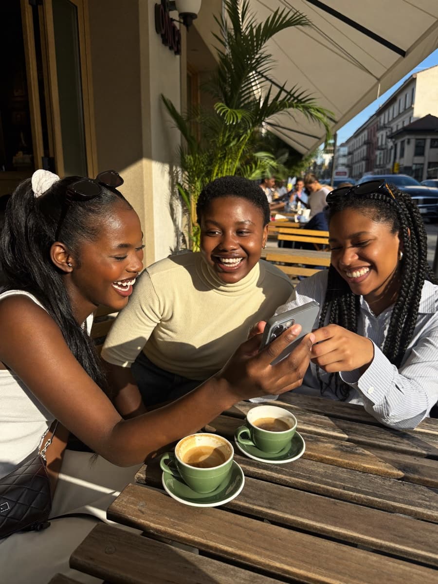 Three young friends laughing at a cafe, looking at a phone together